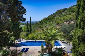 A swimming pool with lounge chairs, surrounded by trees and a view of a hillside.