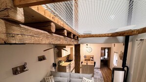 Un espacio habitable moderno y acogedor, con techo de madera, un sofá seccional gris y una pequeña mesa redonda con libros y un control remoto.