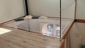 Una habitación con piso de madera, una cama con dosel de mosquitera blanca, un poste negro y una pequeña planta en maceta.