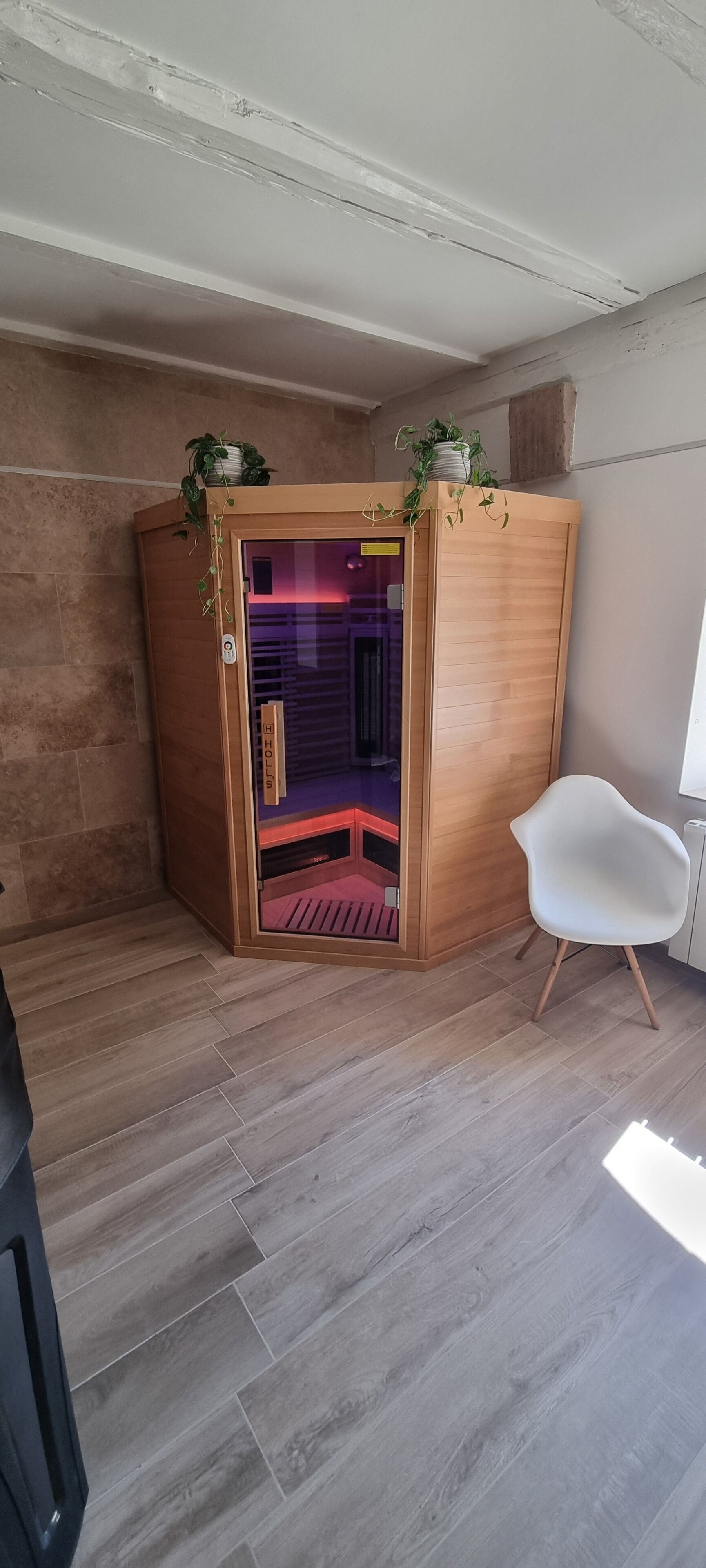 Una habitación con sauna, paredes de madera, una silla blanca y una planta en maceta.