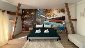Un dormitorio con una cama grande, un sofá blanco, suelo de madera y un mural con un paisaje boscoso.