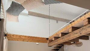 Un interior moderno con una escalera de madera, un banco acolchado blanco y un televisor montado en la pared.