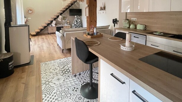 Una cocina moderna con vigas de madera, una isla central y un comedor con una escalera que sube a una buhardilla.