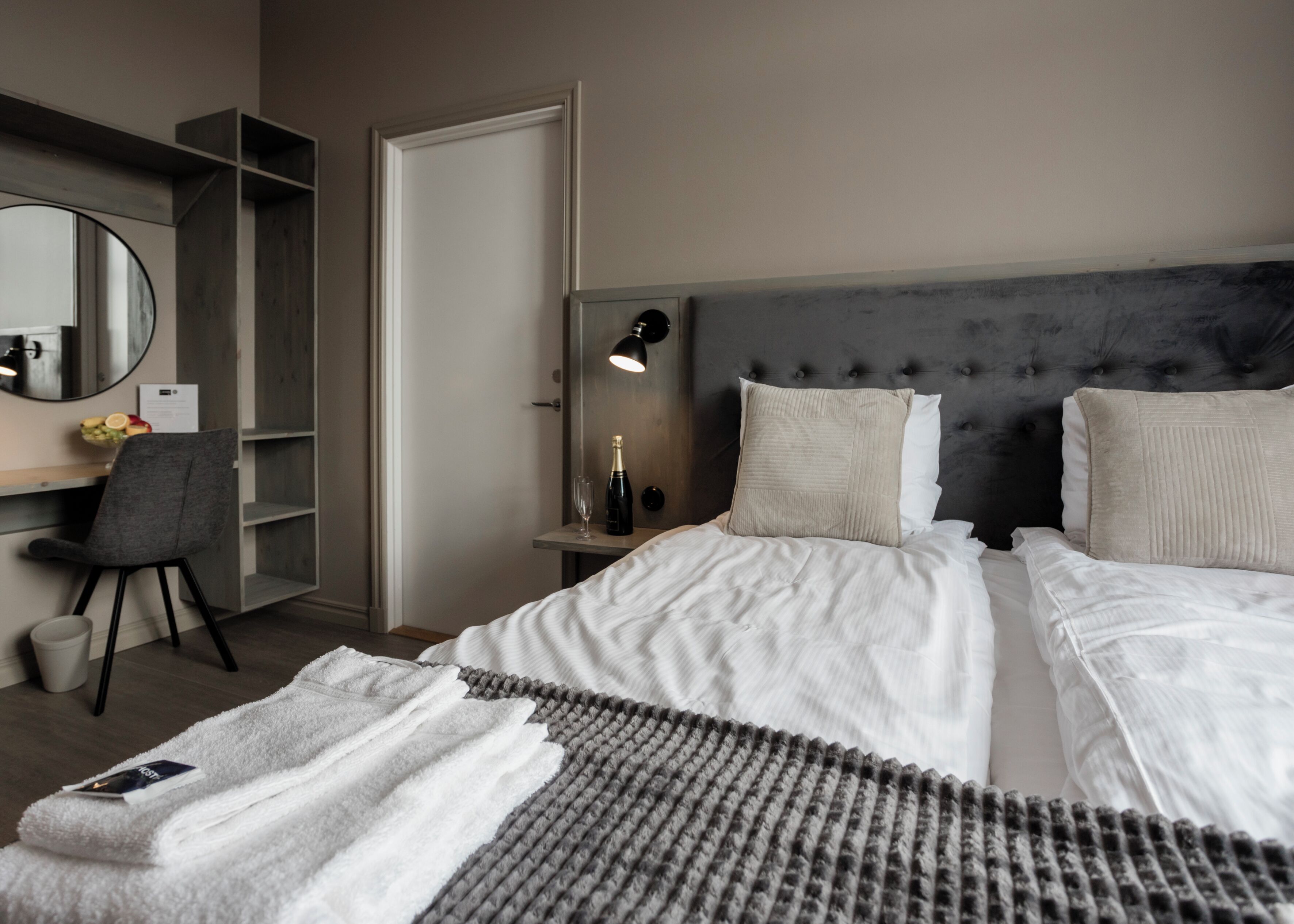 Une chambre d’hôtel moderne, dotée d’un grand lit, d’un bureau avec une chaise, d’un miroir et d’une table de chevet avec une lampe.