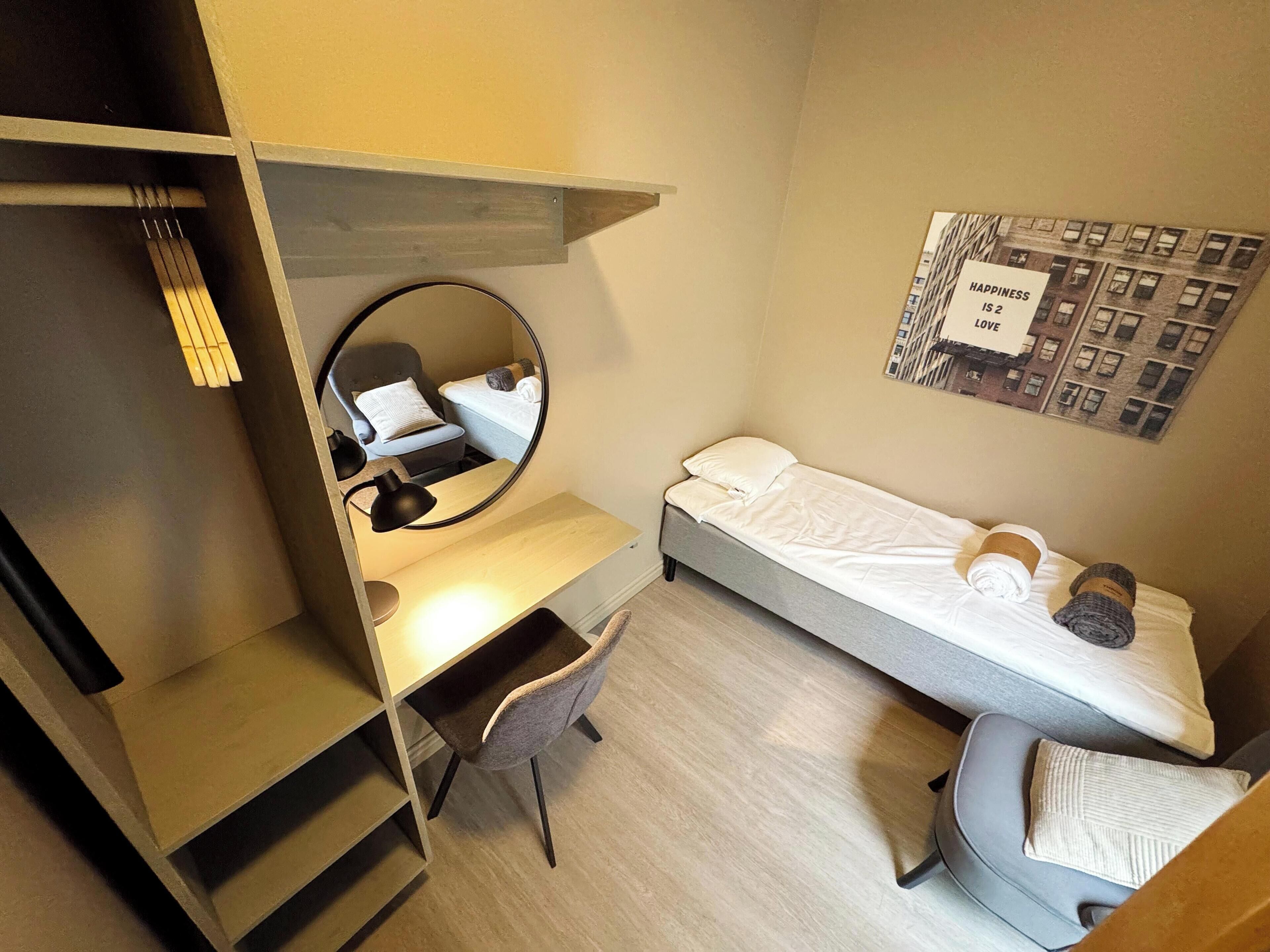 Habitación compacta con cama, escritorio, silla, espejo y estante en la pared.