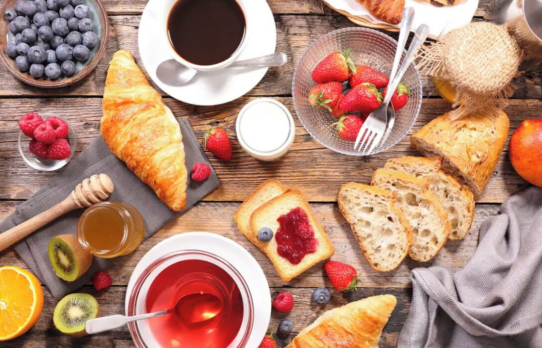 A breakfast spread with croissants, bread, strawberries, blueberries, kiwi, orange, honey, and coffee.