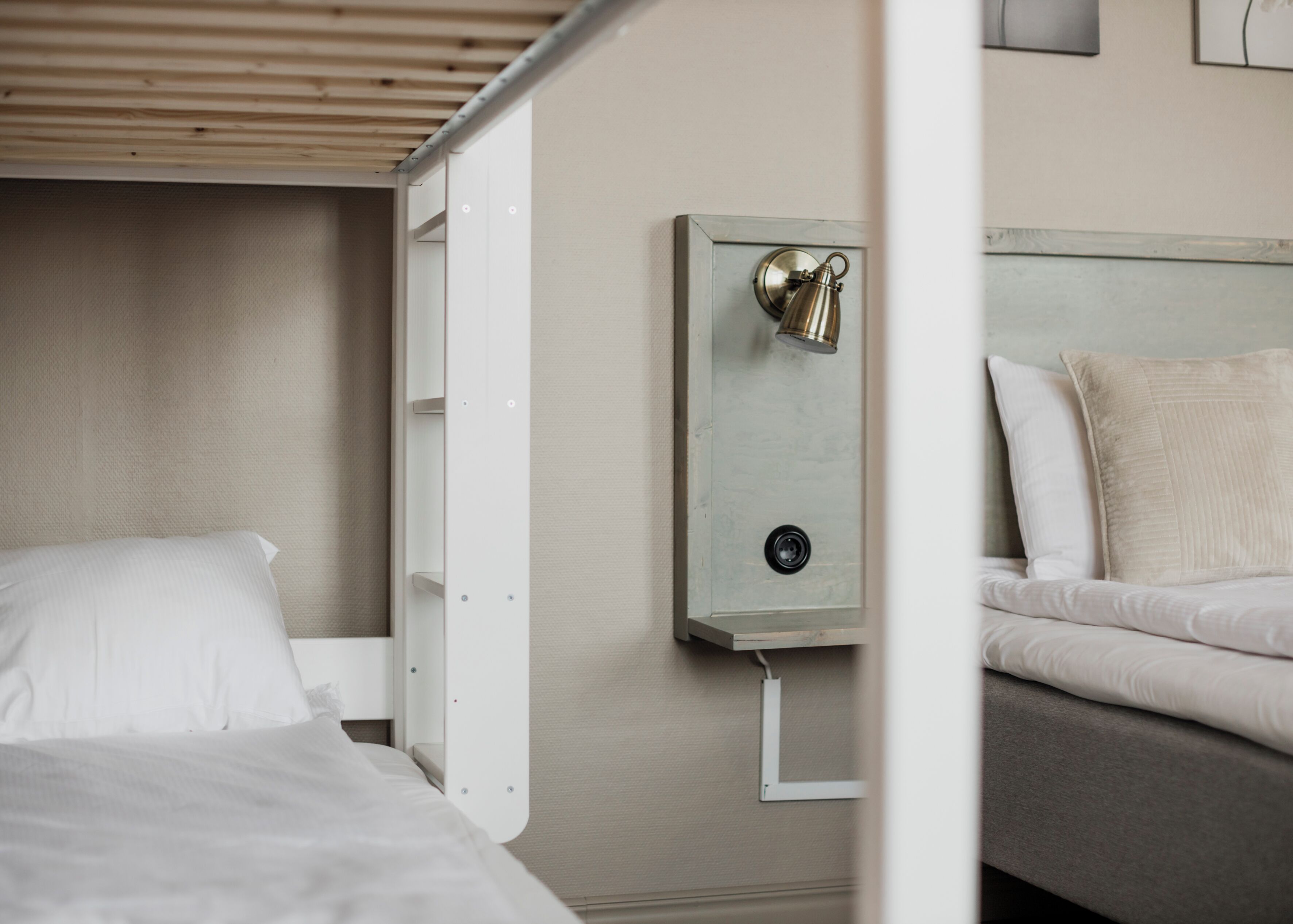 Quarto de hotel com cama de solteiro, mesa de cabeceira com luminária e luminária fixada na parede.
