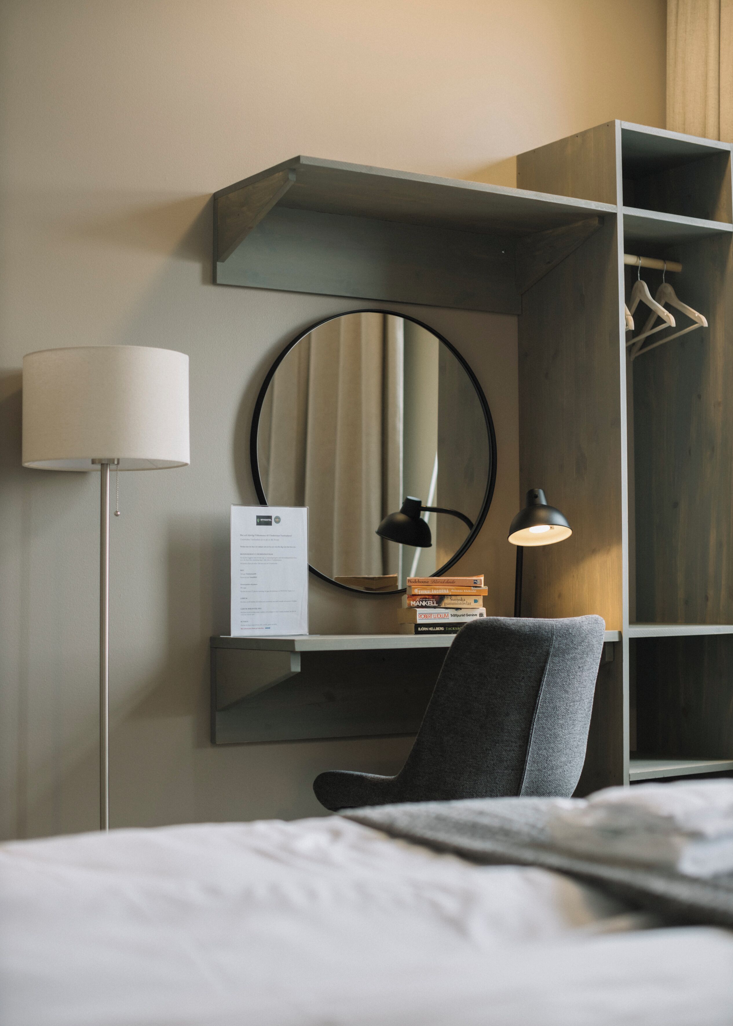 A hotel room with a bed, a desk with a lamp, a mirror, and a wardrobe.