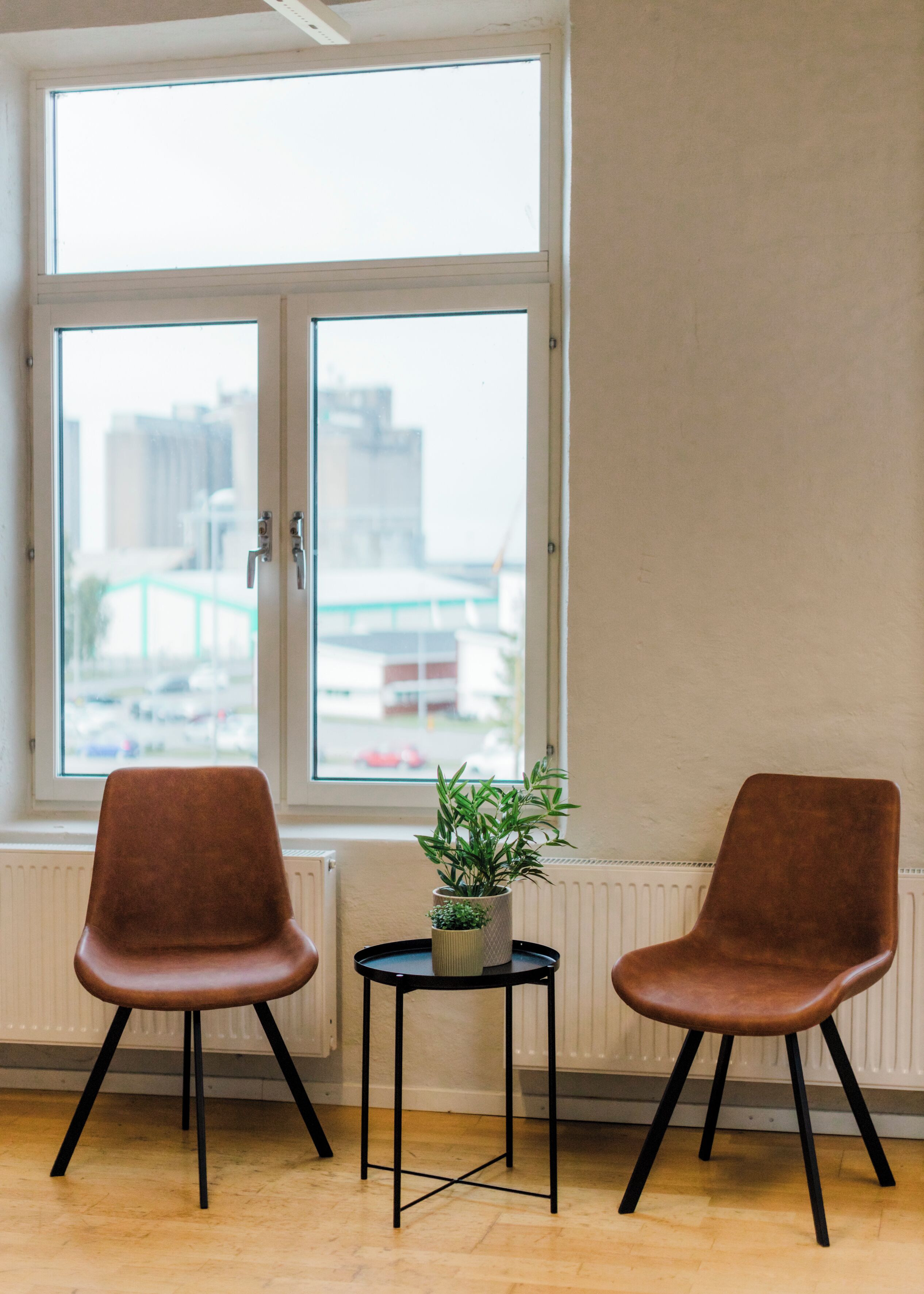 Dos sillas marrones con patas negras, una mesita pequeña negra y una planta en maceta color beige.