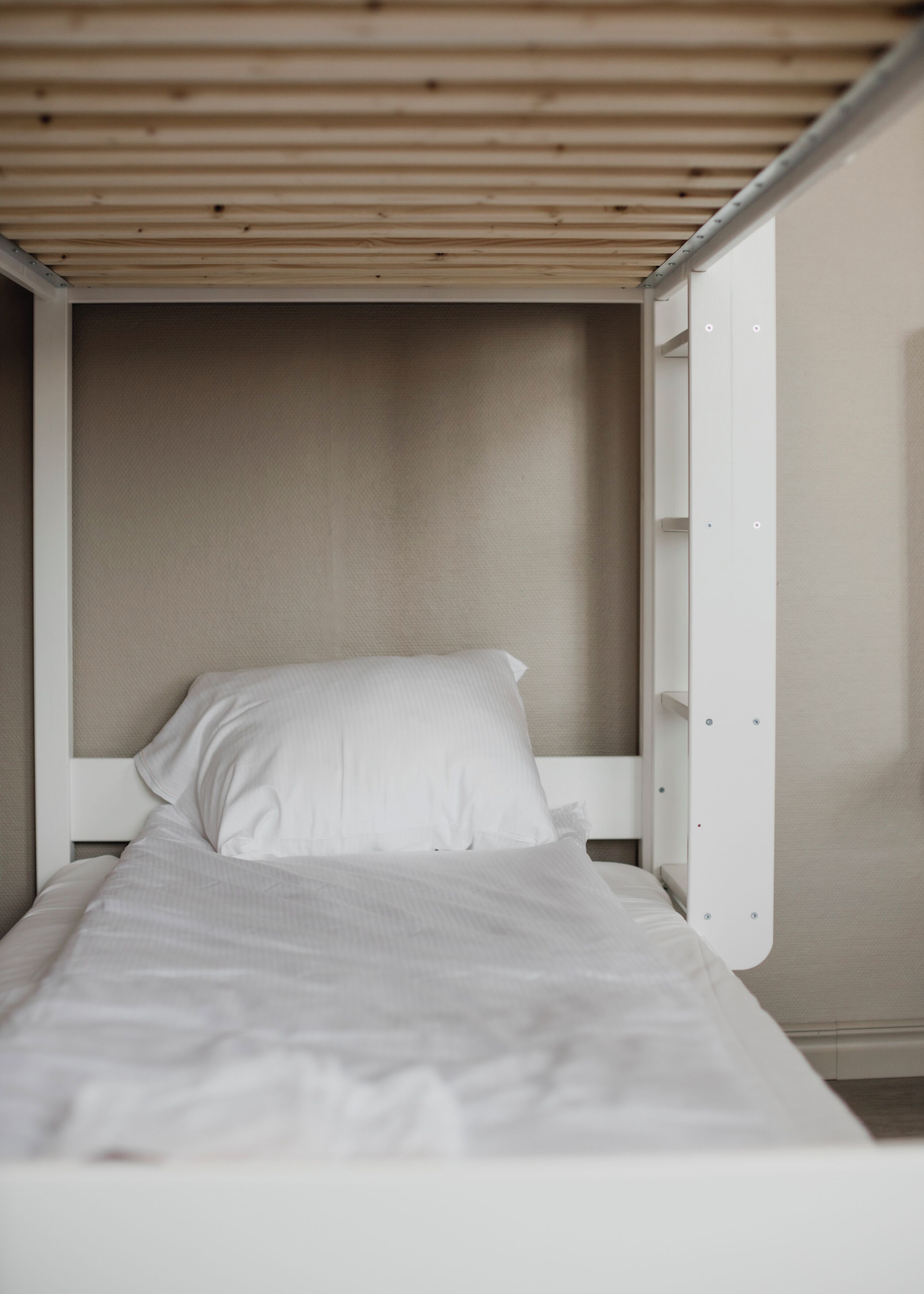 A single bed with white bedding in a room with a wooden ceiling and white walls.