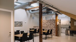 A modern meeting room with a brick accent wall, exposed ductwork, and a kitchen area in the background. - My Hostel Lidköping (Lidköping)