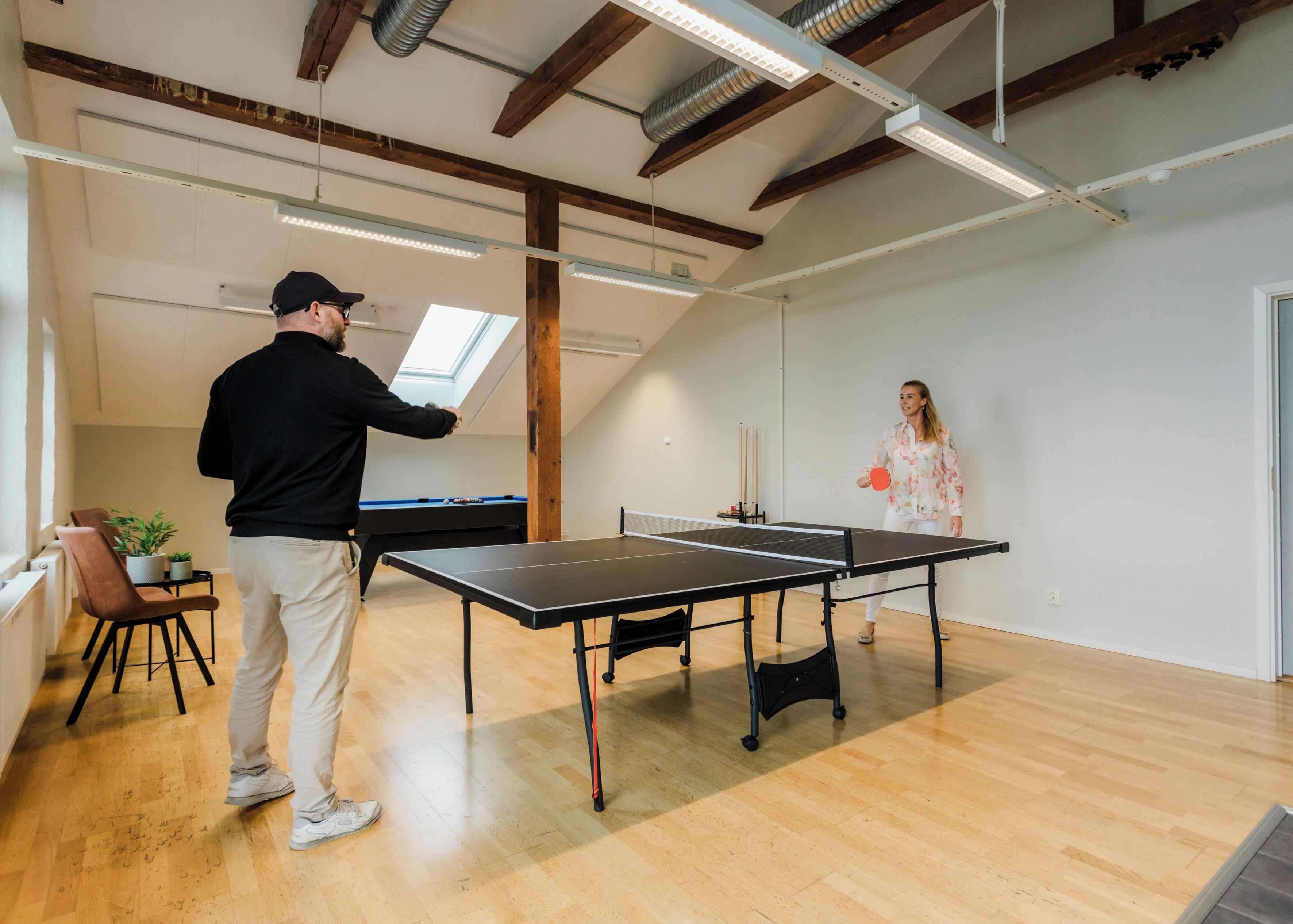 Una mesa de ping pong en una habitación con pisos de madera y techo inclinado.