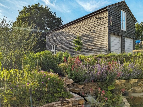 A rustic wooden building with a stone wall and a variety of colorful flowers in the foreground. - Relax, switch off, and reconnect in this inviting Shropshire studio. (Shrewsbury)