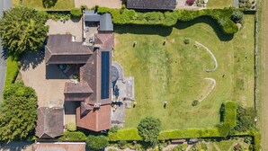 Vue aérienne d’une propriété dotée d’une grande pelouse, d’une piscine et d’un bâtiment dont le toit est en pente.