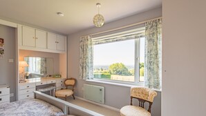 Une chambre à coucher comprenant un lit, une coiffeuse avec un miroir, un radiateur, une fenêtre avec des rideaux et une vue sur l’extérieur.