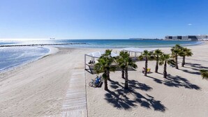 A beach with a wooden boardwalk, palm trees, and beach umbrellas. - Apt Charme Exceptionnel Alicante (Alacant)