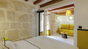A bedroom with stone walls, a bed with white bedding, a yellow sofa, and a small round table.