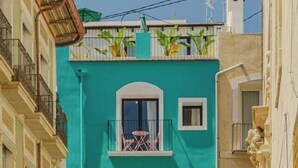 A two-story building with a teal facade, balconies with railings, and a small window on the ground floor. - Apt Charme Exceptionnel Alicante (Alacant)