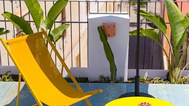 A yellow lounge chair and a small yellow table with a decorative item on it, set on a balcony with a green umbrella. - Apt Charme Exceptionnel Alicante (Alacant)