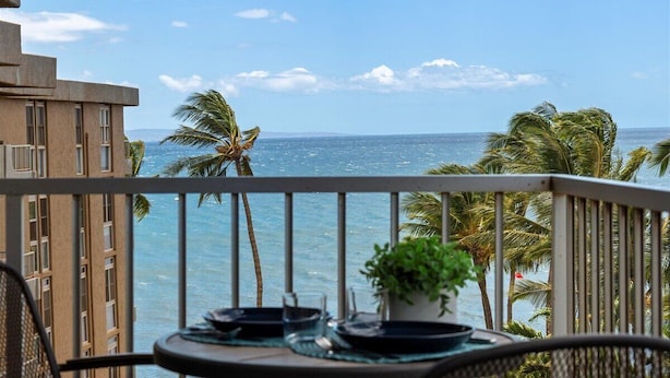 Un balcone con un tavolo apparecchiato per mangiare, affacciato su una spiaggia con palme e l'oceano.