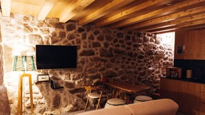 A cozy room with a stone wall, a television, a wooden table, and a sofa.