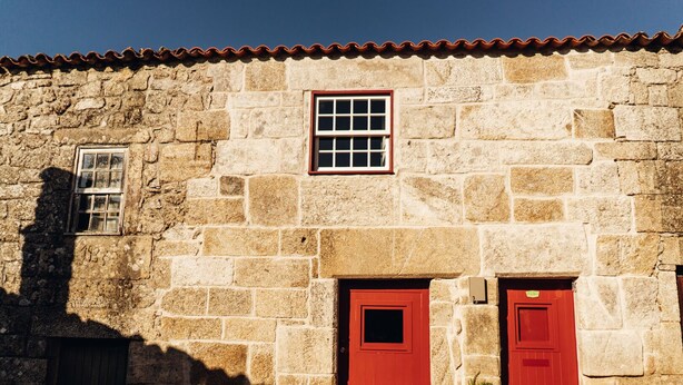 A stone building with two red doors and a small window.