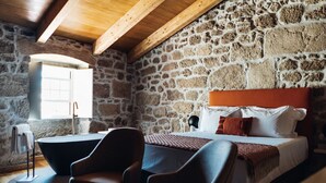 Een slaapkamer met een stenen muur, een bed met witte beddengoed, een houten hoofdbord en een zwart bad.