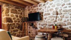 A stone-walled room with a wooden table and chairs, a television mounted on the wall, and a small potted plant on the table.