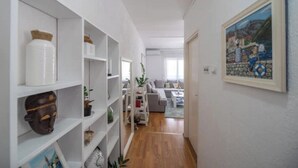 A hallway with white shelving units, a painting on the wall, and a living area with a sofa and coffee table.