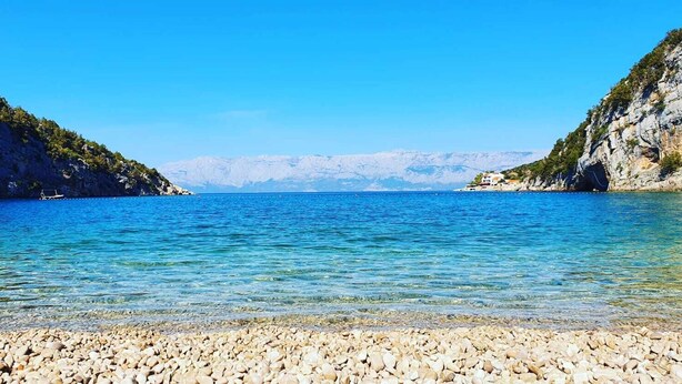 Een kiezelstrand met helderblauw water en rotsachtige kliffen.