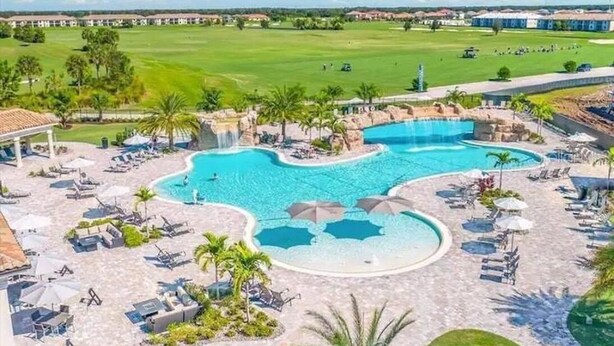 Ein Resort mit einem großen Poolbereich, zahlreichen Liegestühlen und einem Golfplatz im Hintergrund.