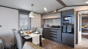 A modern kitchen with a built-in oven, microwave, and gas stove. There is a dining area with a table set for two and a sofa. - 2 bedroom accommodation in St Andrews (St Andrews)