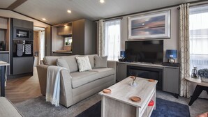 A modern living room with a sofa, coffee table, TV, and kitchen area. - 2 bedroom accommodation in St Andrews (St Andrews)