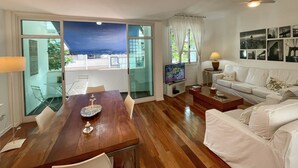 A spacious living room with a wooden dining table, a white sofa, and a ceiling fan. - Prédio Vinicius  (Rio de Janeiro)