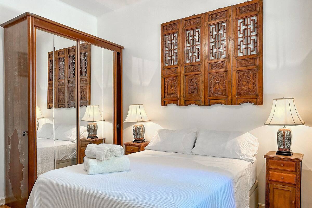 Quarto de hotel com uma cama grande, duas mesas de cabeceira com luminárias, um guarda-roupa de madeira e um painel decorativo de madeira na parede.