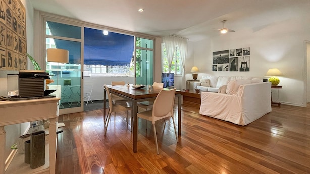 A spacious living area with a wooden floor, a dining table, a sofa, and a TV. - Prédio Vinicius  (Rio de Janeiro)
