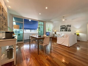 A spacious living area with a wooden floor, a dining table, a sofa, and a TV. - Prédio Vinicius  (Rio de Janeiro)