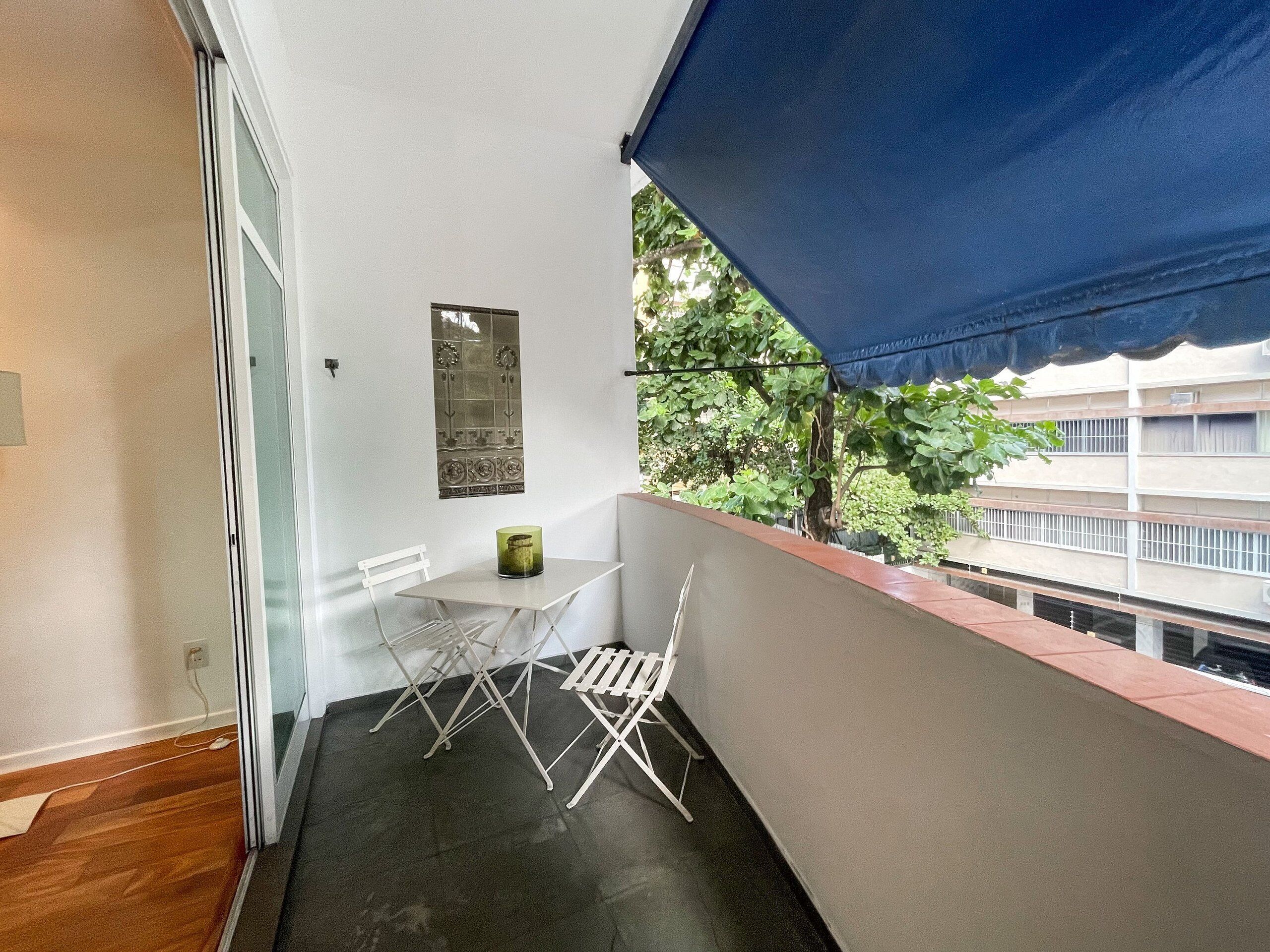Een balkon met een witte klapstoel, een kleine tafel en een blauw zonnescherm.