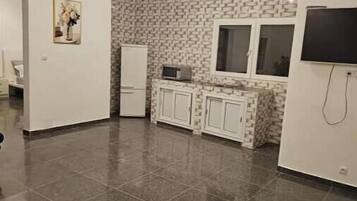 A modern kitchen with a tiled floor, white cabinets, a built-in microwave, and a TV mounted on the wall.