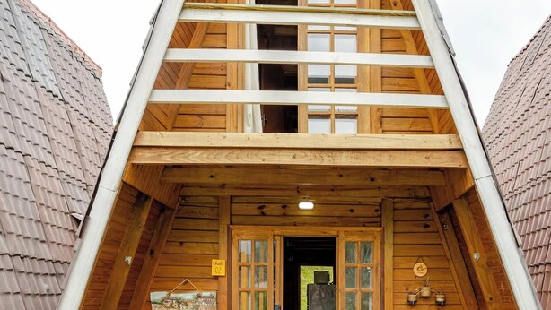 A wooden A-frame building with a covered porch, two chairs, and a small table. - Chale 2 Familia (Angra dos Reis)