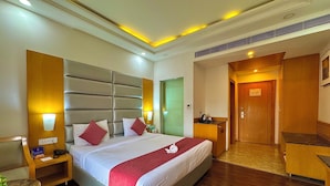 A hotel room with a large bed, bedside tables, a desk, and a door. - Comfort Hotel GMS Grand  (Dehradun)
