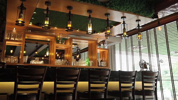 A bar area with wooden chairs, hanging pendant lights, and a green wall. - Comfort Hotel GMS Grand  (Dehradun)
