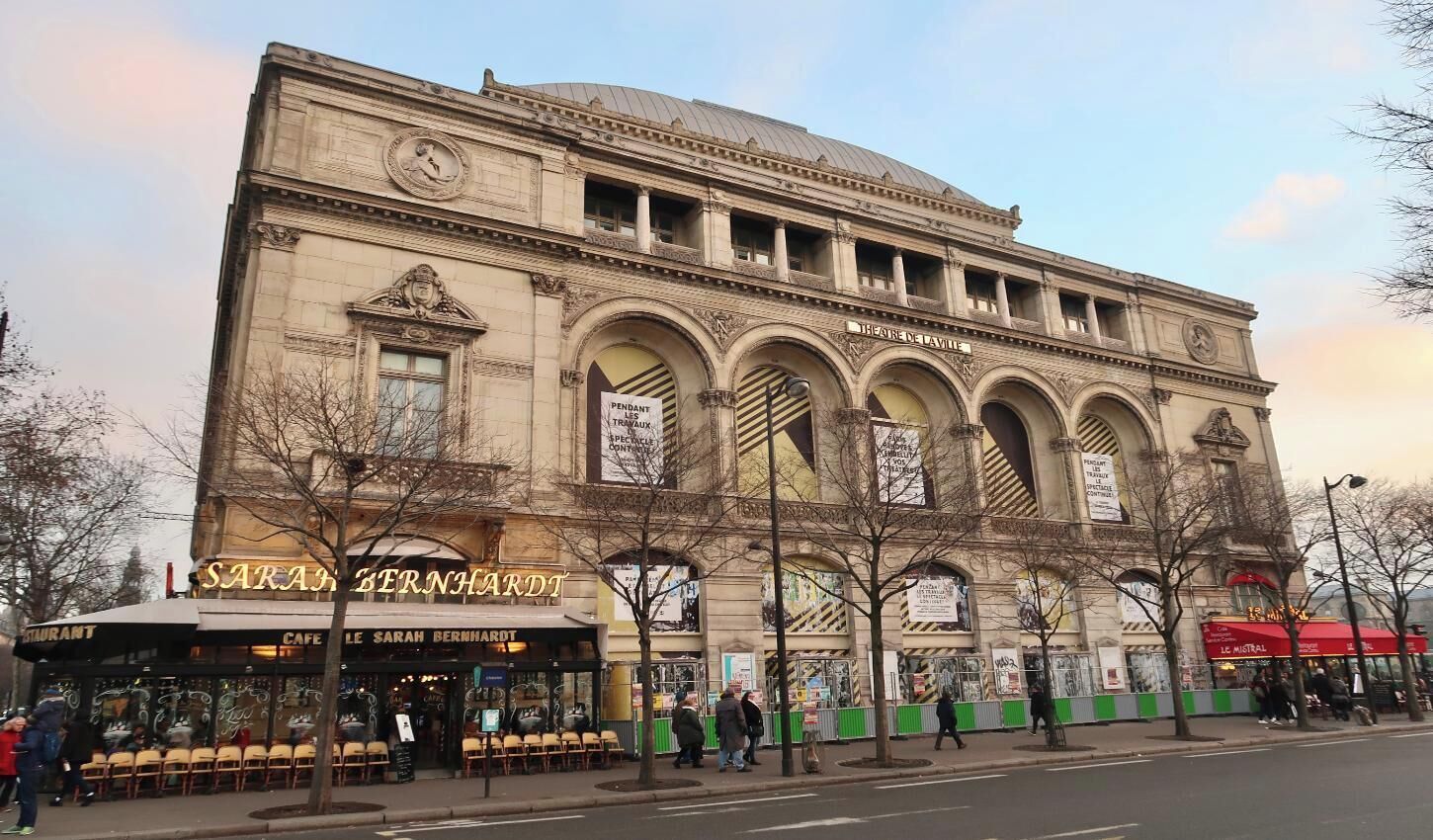 A historic building with a clock tower, arched windows, and a cafe named 'SARAH BERNHARDT' at the ground level.