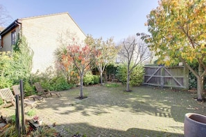 A paved backyard with a brick patio, wooden chairs, and a wooden fence. - 4 BR & 2 Bathroom House Parking Garden St Neots Town Centre (St Neots)