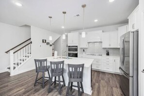 A modern kitchen with white cabinetry, a central island with bar stools, and a stainless steel refrigerator.