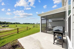 A covered outdoor area with a grill, a view of a green field, and a building with a garage door. - Golf-range View- Slps 11-Beach Shuttle-Grill- Pool (North Myrtle Beach)