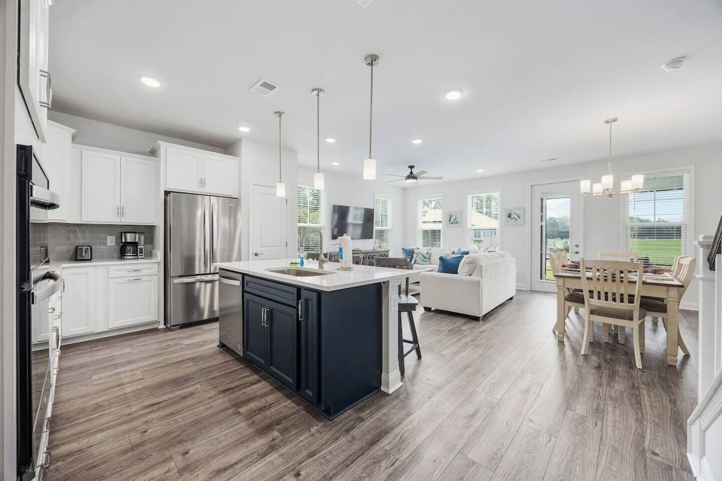 A modern kitchen with a central island, white cabinetry, and a dining area with a wooden table and chairs.