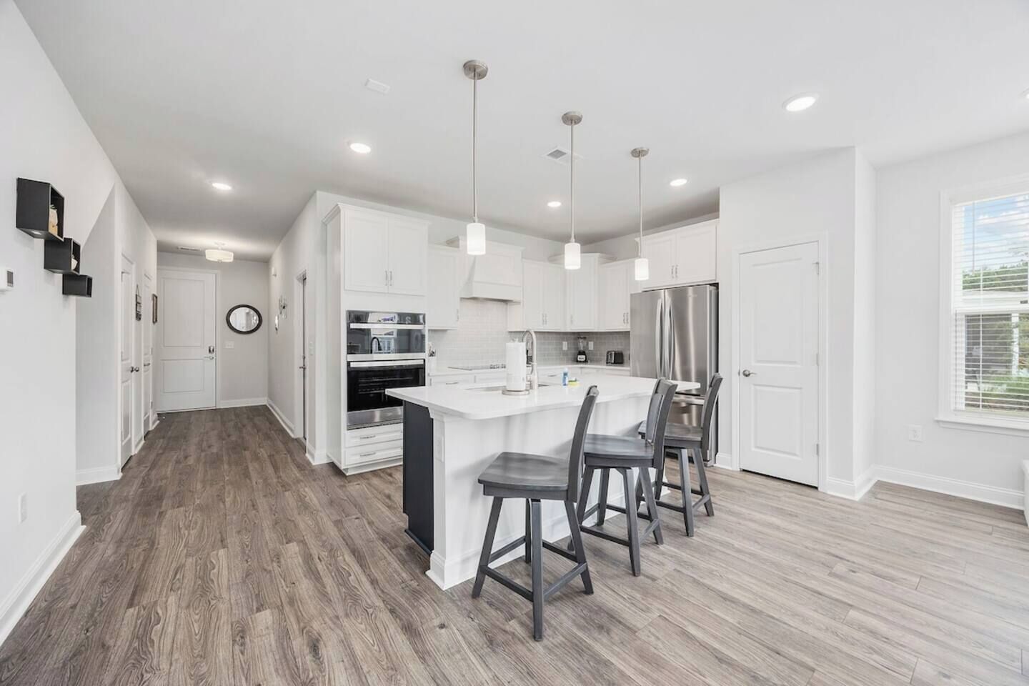 Una cocina moderna con armarios blancos, una isla central con taburetes y un refrigerador de acero inoxidable.