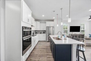 A modern kitchen with white cabinets, stainless steel appliances, and a large island with a sink. - Golf-range View- Slps 11-Beach Shuttle-Grill- Pool (North Myrtle Beach)