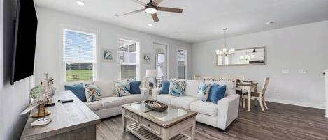 A modern living room with a sectional sofa, a coffee table, and a dining area with a wooden table and chairs.